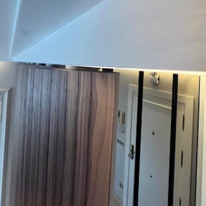 May include: Interior shot featuring a wooden cabinet with vertical grain, a white door, and a mirror with black trim. The ceiling is white with recessed lighting, creating a modern aesthetic.