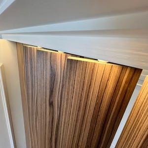 May include: Wooden panels with a zebrawood grain pattern are installed on a wall. The panels are a warm brown color with dark brown streaks. The panels are installed under a white ceiling.