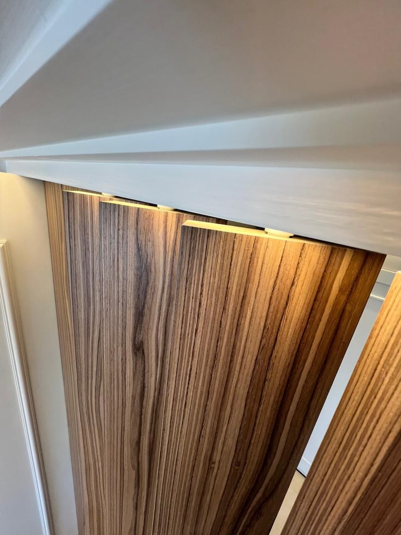 May include: Wooden panels with a zebrawood grain pattern are installed on a wall. The panels are a warm brown color with dark brown streaks. The panels are installed under a white ceiling.