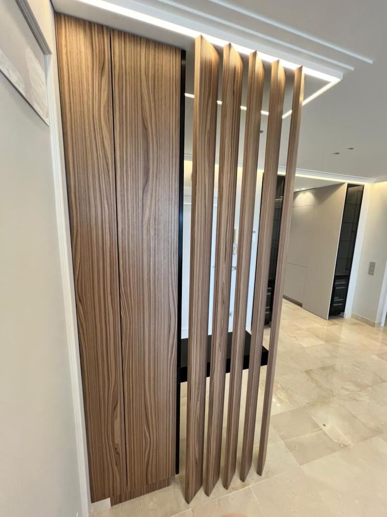 May include: A modern interior design featuring a built-in wooden cabinet with vertical grain and a series of vertical wooden slats. The cabinet and slats are a warm brown color, creating a natural and inviting aesthetic. The design is complemented by a white ceiling.