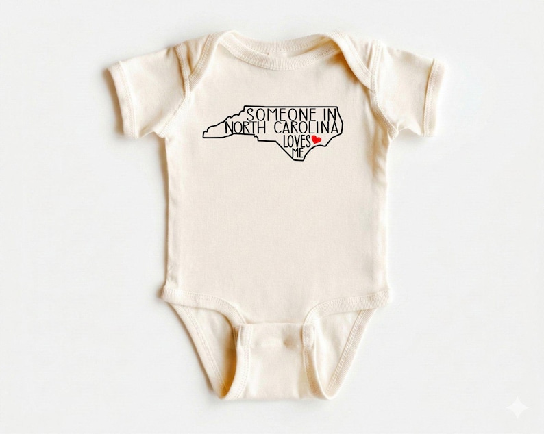 Body para bebé con el mensaje "Alguien en Carolina del Norte me ama", camiseta adorable para bebé, regalos para baby shower, camiseta para bebé con el mensaje "Amado", body para bebé con el estado, camiseta natural para bebé. imagen 1
