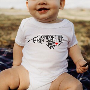 Body para bebé con el mensaje "Alguien en Carolina del Norte me ama", camiseta adorable para bebé, regalos para baby shower, camiseta para bebé con el mensaje "Amado", body para bebé con el estado, camiseta natural para bebé. imagen 2