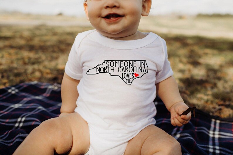 Body para bebé con el mensaje "Alguien en Carolina del Norte me ama", camiseta adorable para bebé, regalos para baby shower, camiseta para bebé con el mensaje "Amado", body para bebé con el estado, camiseta natural para bebé. imagen 2
