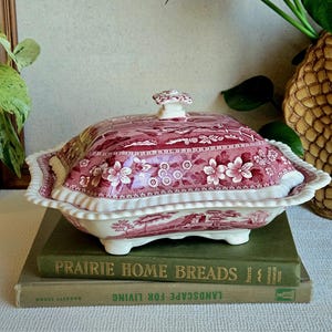 May include: A rectangular ceramic covered serving dish featuring a deep red and white transferware pattern of floral motifs and a landscape scene. The dish has a scalloped edge, four small feet, and a central handle on the lid.