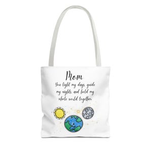 Op de afbeelding: Witte draagtas met een Mom-afbeelding. De tas heeft de tekst "Mom, You light my days, guide my nights, and hold my whole world together." Het ontwerp bevat illustraties van de zon, de aarde en de maan.
