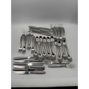 May include: A collection of stainless steel silverware, including forks, knives, and spoons. The silverware has a textured handle design. The arrangement includes multiple sets of each utensil, suitable for a large gathering or formal dining.
