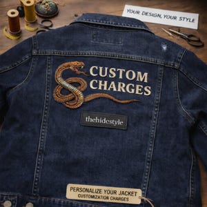 Pode incluir: Casaco de ganga azul escuro com um patch de cobra detalhado e as palavras "CUSTOM CHARGES". O casaco também apresenta um pequeno patch preto com "thehidestyle" e uma etiqueta que diz "PERSONALIZE YOUR JACKET CUSTOMIZATION CHARGES".