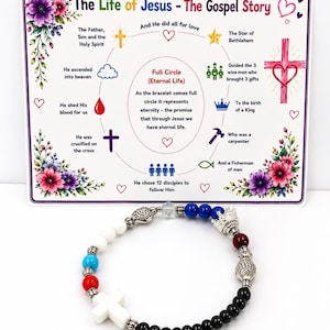 May include: A beaded bracelet featuring a white cross charm, black, red, blue, and white beads, a silver crown, and a fish charm. It is displayed in front of a card titled The Life of Jesus - The Gospel Story, which illustrates the meaning of the beads.