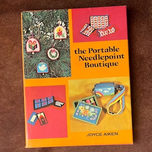May include: A vintage book cover titled "the Portable Needlepoint Boutique" by Joyce Aiken. The cover features images of needlepoint projects, including Christmas ornaments and small bags with floral and geometric designs. The cover is orange and red.