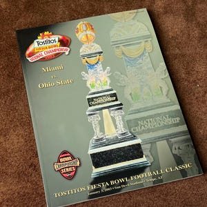 May include: A 2003 Tostitos Fiesta Bowl Football Classic programme. The cover displays the National Championship trophy and logos for Tostitos and the Bowl Championship Series. The game was between Miami and Ohio State.