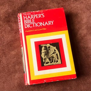 Könnte beinhalten: Ein Buch mit dem Titel "THE NEW HARPER'S BIBLE DICTIONARY" mit rotem Einband und gelb-weißen Rändern. Das Cover zeigt eine Illustration in einem schwarzen Quadrat. Das Buch ist leicht abgenutzt, mit dem Titel in weißen Buchstaben.