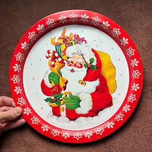 Puede incluir: Bandeja de servir navideña roja y blanca con un diseño festivo que presenta a Papá Noel sosteniendo una bolsa de regalos. La bandeja tiene un borde de copo de nieve.
