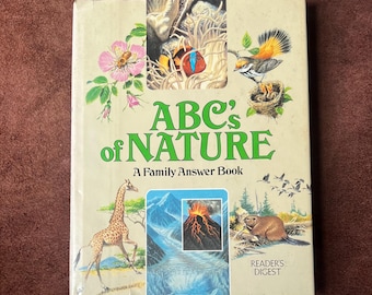 May include: A vintage hardcover book titled "ABC's of Nature" with illustrations of a giraffe, volcano, and birds. The cover features the text "A Family Answer Book" and the Reader's Digest logo. The book has a cream-colored background.