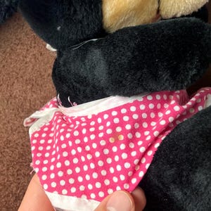 Pu&ograve; includere: Un peluche con pelliccia nera, orecchie color beige e un vestito rosa a pois bianchi con rifiniture bianche. Il design del giocattolo &egrave; visibile, con l'abito e la pelliccia come elementi pi&ugrave; importanti.