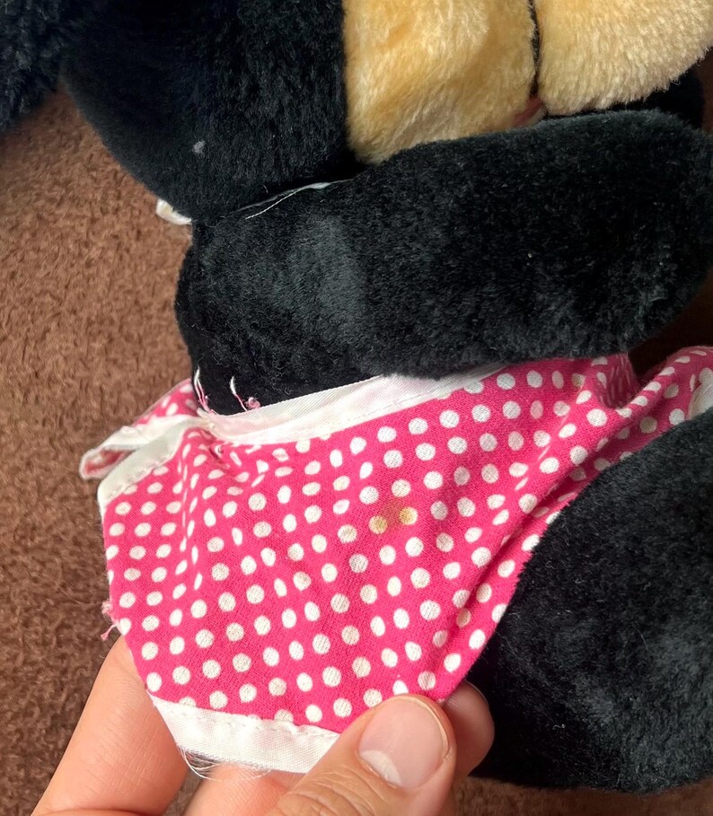 Pu&ograve; includere: Un peluche con pelliccia nera, orecchie color beige e un vestito rosa a pois bianchi con rifiniture bianche. Il design del giocattolo &egrave; visibile, con l'abito e la pelliccia come elementi pi&ugrave; importanti.