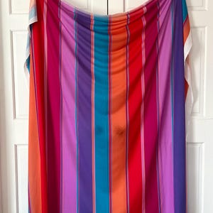 Op de afbeelding: Een levendige stof met verticale strepen in een spectrum van kleuren, waaronder rood, oranje, roze, paars en turquoise. De stof hangt tegen een witte achtergrond en toont zijn gedurfde en kleurrijke ontwerp. Dit textiel is geschikt voor diverse knutselprojecten.
