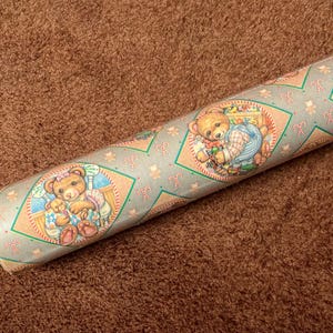 Puede incluir: Un rollo de papel de regalo con fondo azul y verde con un patrón repetido de bastones de caramelo y osos de peluche. Los osos de peluche llevan atuendos azules y blancos y sostienen juguetes.