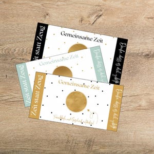 Może przedstawiać: Trzy prostokątne karty ze złotymi, czarnymi i jasnoniebieskimi akcentami. Karty zawierają tekst "Gemeinsame Zeit" i "Zeit statt Zeug". Widoczny jest również złoty okrąg i wzór w kropki.