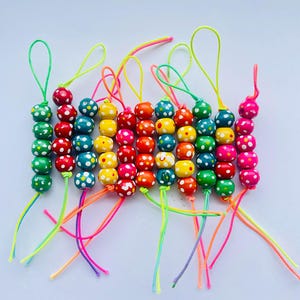 May include: A collection of colorful beaded keychains. Each keychain features a string of wooden beads in various colors, including green, red, yellow, orange, blue, and pink. The beads are decorated with white polka dots. Each keychain has a loop at the top.
