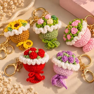 Pode incluir: Cinco porta-chaves em forma de ramo de flores em croché com argolas e fechos de mosquetão em metal dourado. Cada um apresenta uma base redonda, um rebordo branco com folhos e flores de fio coloridas em amarelo, rosa, vermelho e roxo.