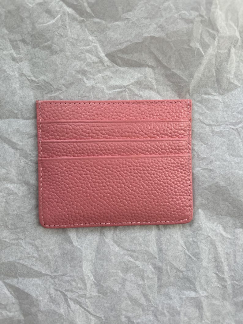 May include: A pink leather card holder with multiple card slots. The card holder is rectangular and has a textured surface. The stitching is visible around the edges.
