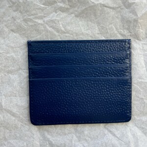 May include: A navy blue card holder with a textured surface. The card holder has multiple slots for cards and a rectangular shape. The card holder is made of a leather-like material.
