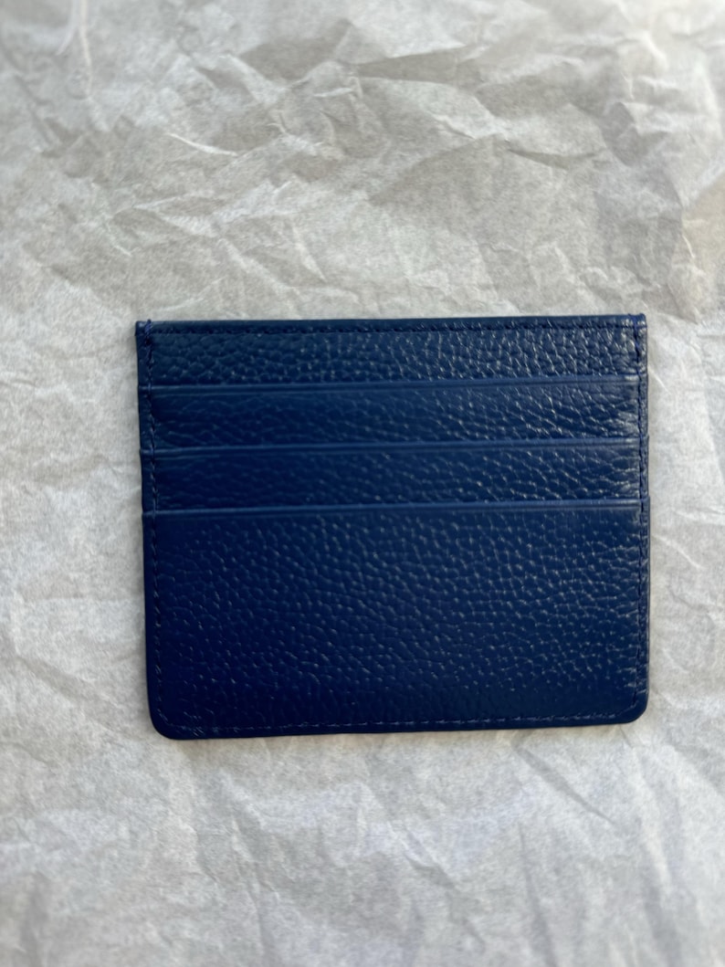 May include: A navy blue card holder with a textured surface. The card holder has multiple slots for cards and a rectangular shape. The card holder is made of a leather-like material.