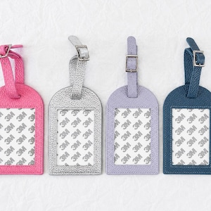 May include: Four rectangular luggage tags with rounded tops in pink, silver, lavender, and dark blue. Each tag features a textured surface, a clear window with a 3M branded protective film, and an adjustable strap with a silver metal buckle.