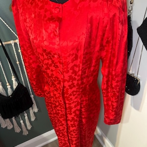 Peut inclure: Une robe rouge vif avec un motif en forme de c&oelig;ur. La robe &agrave; manches longues pr&eacute;sente une encolure ronde et une fermeture &agrave; un seul bouton. La robe est pr&eacute;sent&eacute;e sur un mannequin noir.