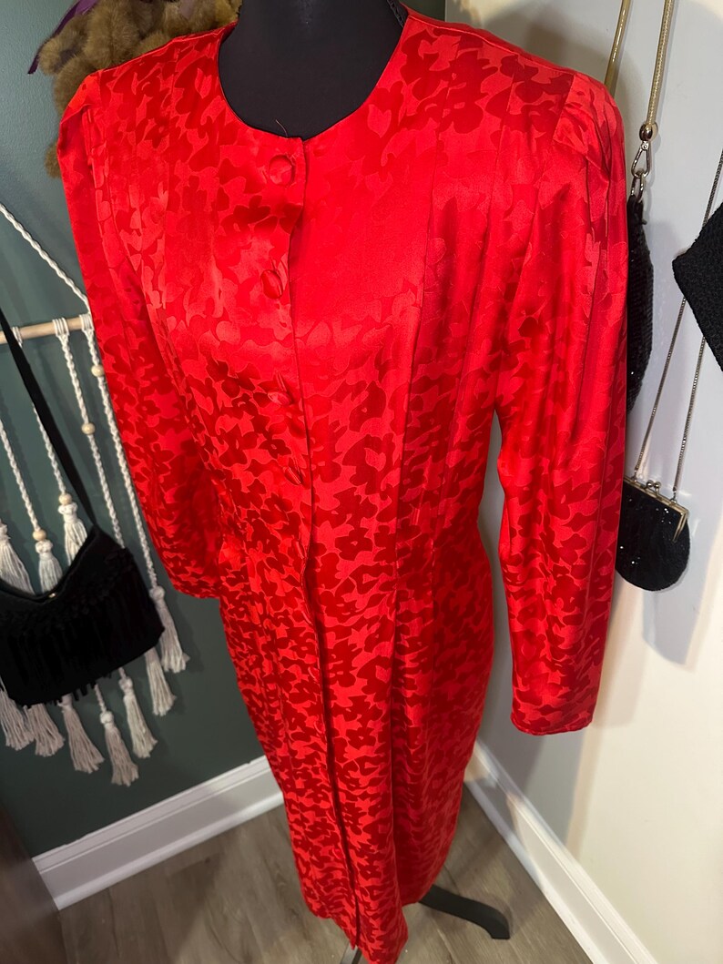 Peut inclure: Une robe rouge vif avec un motif en forme de c&oelig;ur. La robe &agrave; manches longues pr&eacute;sente une encolure ronde et une fermeture &agrave; un seul bouton. La robe est pr&eacute;sent&eacute;e sur un mannequin noir.