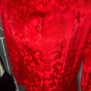 Peut inclure: Une blouse rouge vif &agrave; motifs floraux. Ce haut &agrave; manches longues pr&eacute;sente un col rond et trois boutons visibles. Le tissu a un l&eacute;ger &eacute;clat et le motif floral est l&eacute;g&egrave;rement plus fonc&eacute; que la couleur de base.