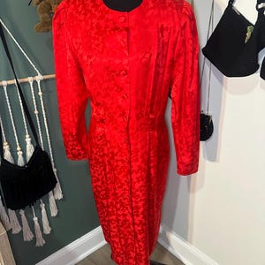 Peut inclure: Une robe rouge vif avec un motif floral subtil. La robe a des manches longues, un devant boutonn&eacute; et un ourlet jusqu'aux genoux. La robe est pr&eacute;sent&eacute;e sur un mannequin noir.