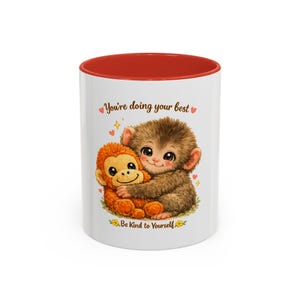 May include: White ceramic mug with a red interior featuring a cartoon illustration of two monkeys hugging. The mug has the text "You're doing your best" and "Be Kind to Yourself" with hearts and stars.