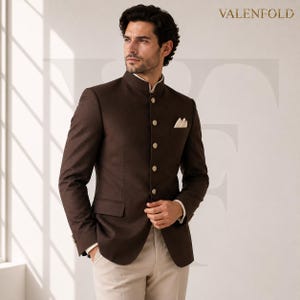 Pode incluir: Um blazer castanho escuro com gola mandarim, cinco botões claros na frente, um bolso no peito com um lenço branco e dois bolsos laterais com aba. O nome da marca VALENFOLD está impresso no canto superior direito da imagem.