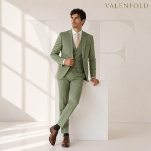Puede incluir: Un traje de tres piezas en color verde apagado. El traje incluye una chaqueta, un chaleco y un pantal&oacute;n. El modelo lleva una camisa blanca y una corbata melocot&oacute;n claro. Zapatos de vestir de cuero marr&oacute;n completan el look. La marca "VALENFOLD" se muestra en la parte superior.