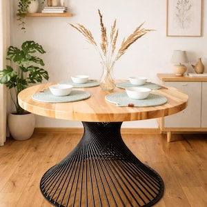 Può includere: Un tavolo da pranzo rotondo in legno con base in metallo nero. Il tavolo è apparecchiato con quattro ciotole bianche, sottopiatti e un vaso di fiori secchi. Una lampada a sospensione intrecciata è appesa sopra il tavolo. Il tavolo ha un diametro di circa 122 cm.
