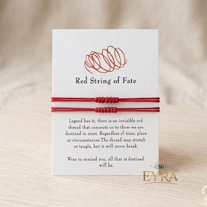 May include: Two red string bracelets mounted on a white rectangular display card. The card features a red line drawing of a tangled knot, the text Red String of Fate, and a paragraph explaining the legend of the red thread of fate.
