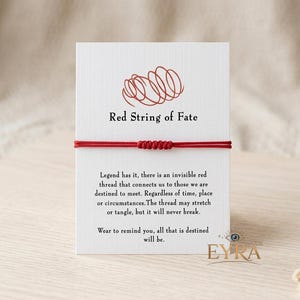 May include: A thin red string bracelet with a central knot, mounted on a white rectangular card. The card features a red line drawing of a tangled thread, the text Red String of Fate, and a printed legend about destiny and connection.
