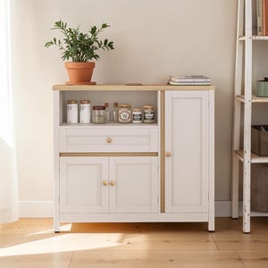 May include: A white cabinet with a light wood top and trim. The cabinet has a drawer, two lower doors, and a single door on the right. A terracotta pot with a green plant sits on top, along with jars and books. The cabinet is on a wooden floor.