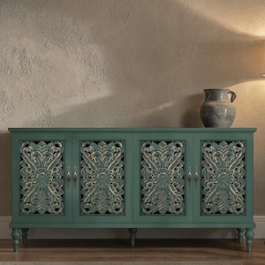 May include: A teal-colored cabinet with four doors, featuring ornate, carved floral designs. The cabinet has a distressed finish and sits on short, rounded legs. A gray ceramic vase rests on top, adding a touch of rustic charm to the piece.