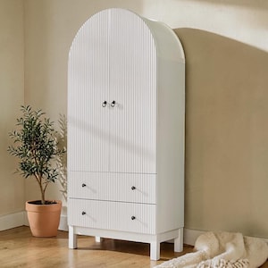 May include: White arched cabinet with vertical ribbed detailing. The cabinet has two doors and two drawers with black knobs. The cabinet is set on four short legs.