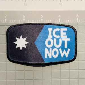 May include: Rectangular patch with a black border. The patch is divided diagonally, with a dark blue section featuring a white star and a light blue section with the words "ICE OUT NOW" in white. The patch is likely for clothing or accessories.