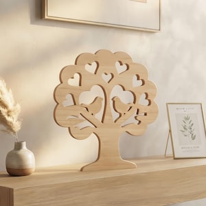 Peut inclure: Une sculpture d'arbre en bois clair présentant un design découpé avec deux oiseaux perchés sur des branches et plusieurs ouvertures en forme de cœur dans la canopée. La pièce a une finition en grain de bois naturel et une base large.