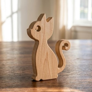 Könnte beinhalten: Eine hellbraune Katzenfigur aus Holz mit glatter, natürlicher Maserung. Die Katze ist im sitzenden Profil dargestellt, mit einer kreisförmigen Aussparung für das Auge und einem geschwungenen, aufrechten Schwanz, der am Ende eine Schleife bildet.