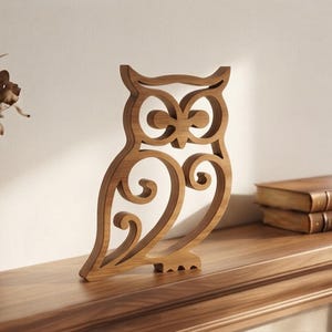 May include: A light brown wooden owl figurine featuring a cutout design with intricate scrollwork patterns throughout the body and head. The owl is standing upright with a flat base, showcasing a natural wood grain texture and smooth finish.