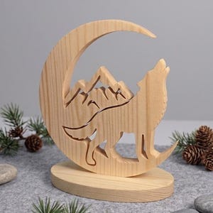 Peut inclure: Sculpture en bois d'un loup hurlant dans un croissant de lune, avec des silhouettes de montagnes. Le loup et la lune sont découpés dans le bois, créant un effet de superposition. La sculpture repose sur une base en bois ronde.
