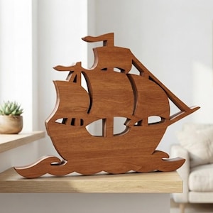 May include: A brown wooden cutout of a sailing ship featuring three distinct sails and a stylized wave base. The object is crafted from a single piece of wood with a visible grain pattern, showcasing a flat, silhouette-style design of a vessel.