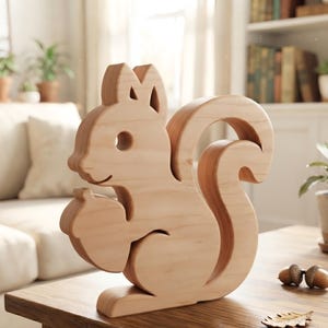 Könnte beinhalten: Eine helle Holzfigur in Form eines Eichhörnchens mit glatter, natürlicher Maserung. Das Eichhörnchen ist sitzend dargestellt und hält eine Eichel in den Vorderpfoten, mit einem geschwungenen Schwanz sowie ausgeschnittenen Details für Auge und Ohr.
