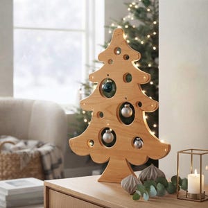 May include: A light-toned wooden Christmas tree cutout featuring circular cutouts of varying sizes. Several small, round ornaments in metallic silver and dark green are suspended within these circular openings. The wooden tree is illuminated by integrated warm white LED lights along its edges.