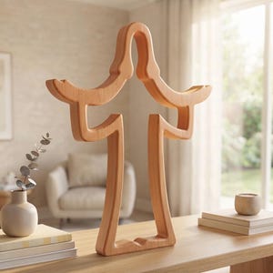 May include: A light brown wooden sculpture featuring a symmetrical, abstract, open-frame design with two curved upper arms and two vertical base supports, standing upright on a flat surface with a smooth, natural wood grain finish.